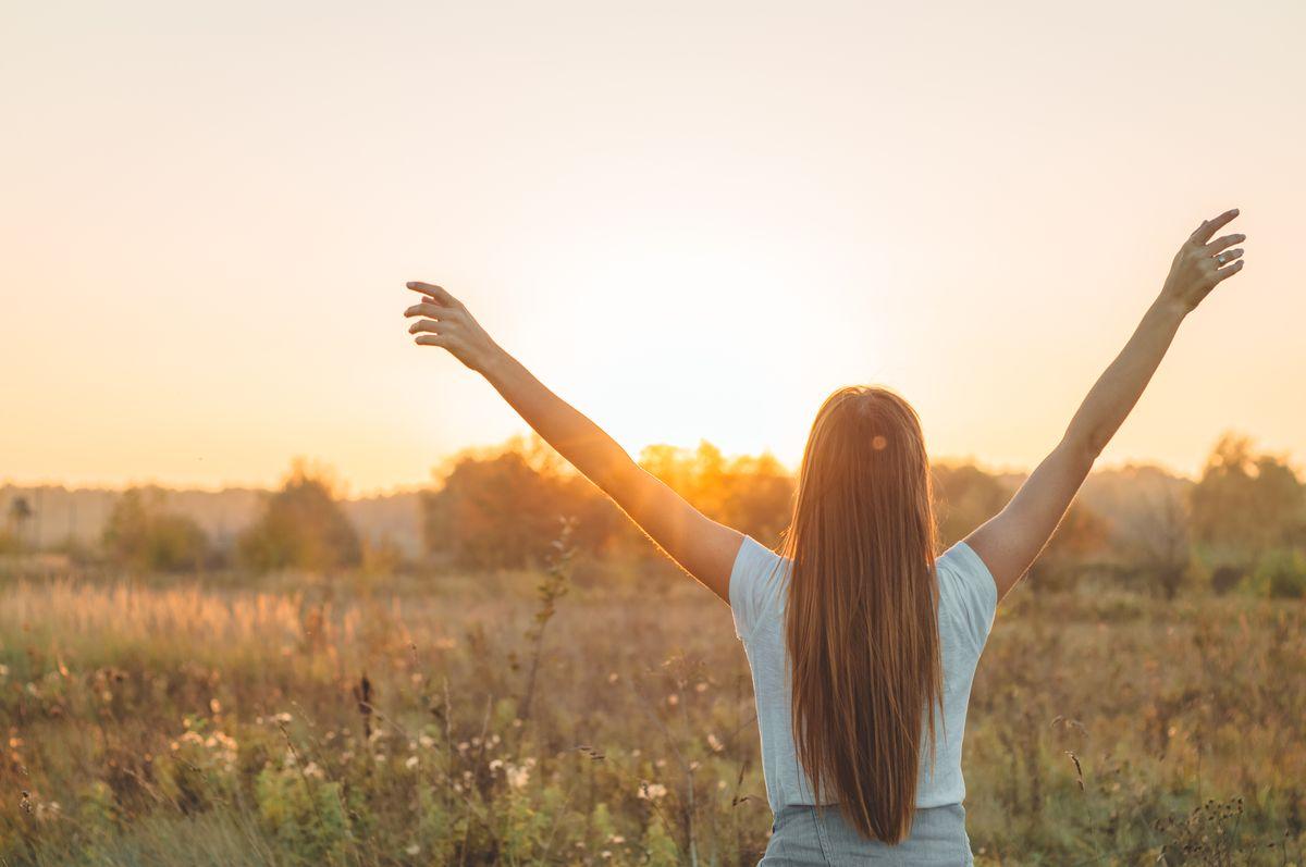 Autumn Girl enjoying nature on the field. Beauty Girl Outdoors raising hands in sunlight rays. Beautiful Teenage Model girl in white dress running on the Field, Sun Light. Glow Sun. Free Happy Woman