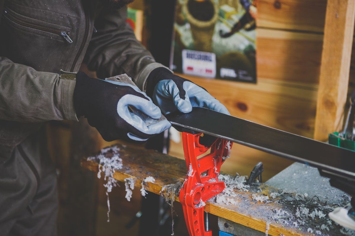 A male worker in a ski service workshop repairs the sliding surface of the skis. Close-up of a hand with a plastic scrapper for removing wax, removing new wax. Theme repair of ski curb.